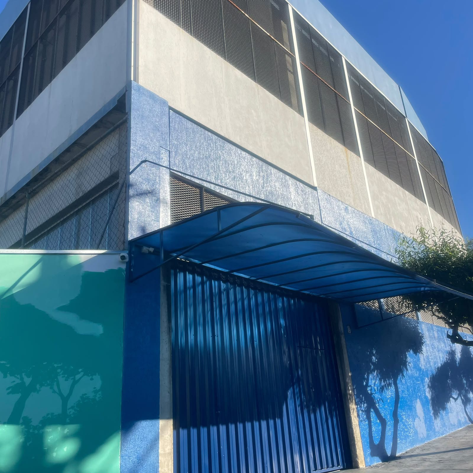 Portão metálico azul de correr e marquise curva em metal na fachada