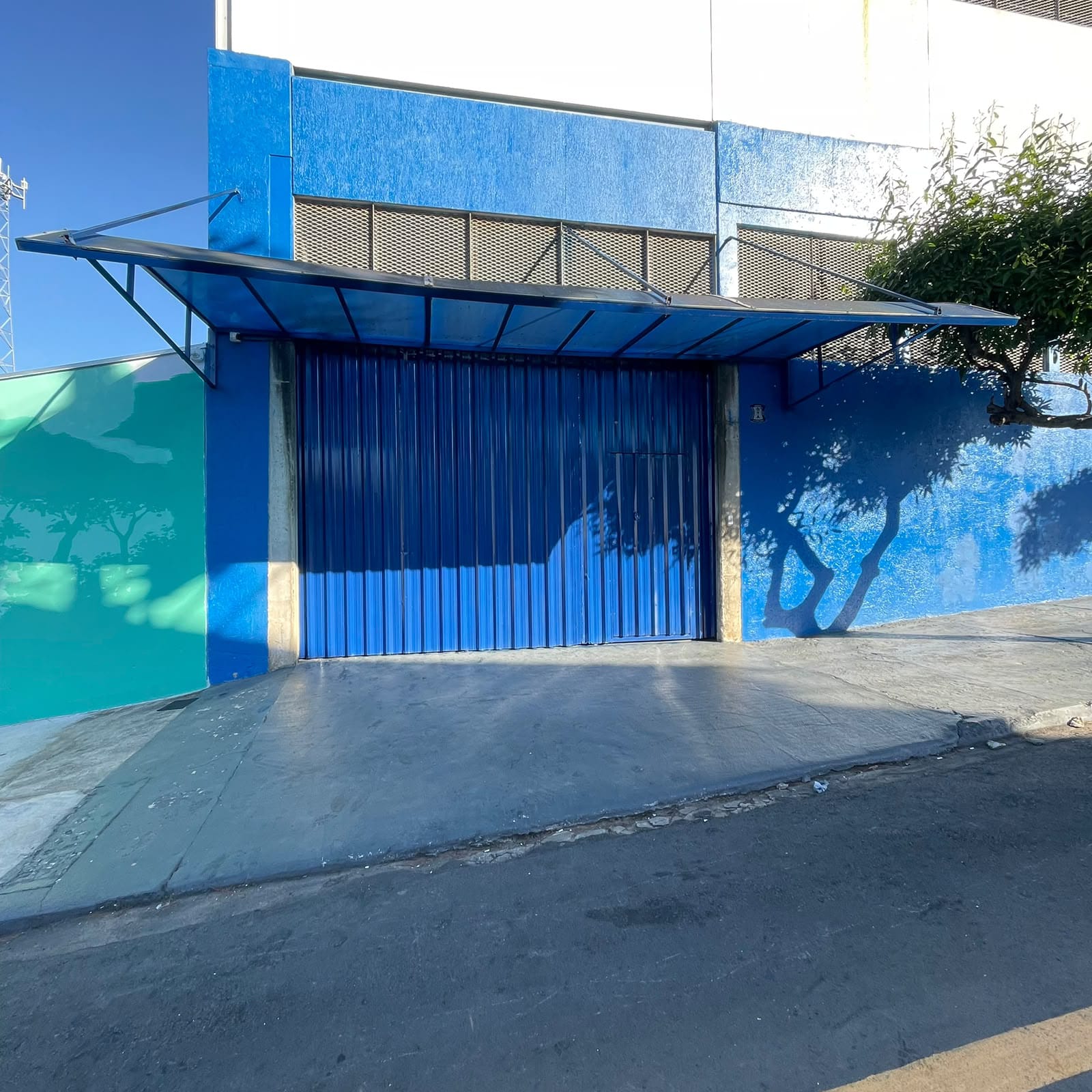 Portão azul de correr e marquise plana em metal na entrada de imóvel